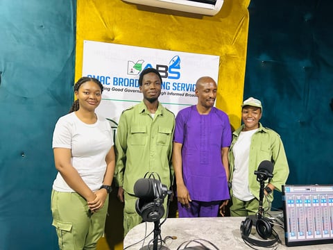 Four people standing in a radio studio with microphones and ABC Broadcasting Services branding visible on the wall